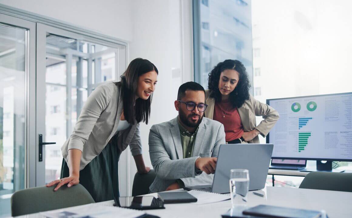 Three colleagues gather around a screen, as one points out an item of interest