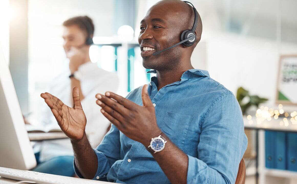 A man in a blue shirt with a headset gestures while speaking