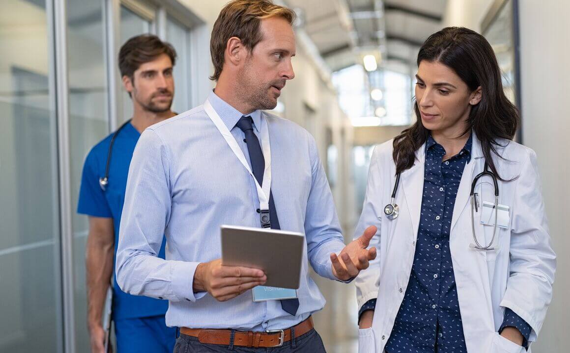 Two doctors walking down a hallway while discussing patient information while a male nurse walks behind them.