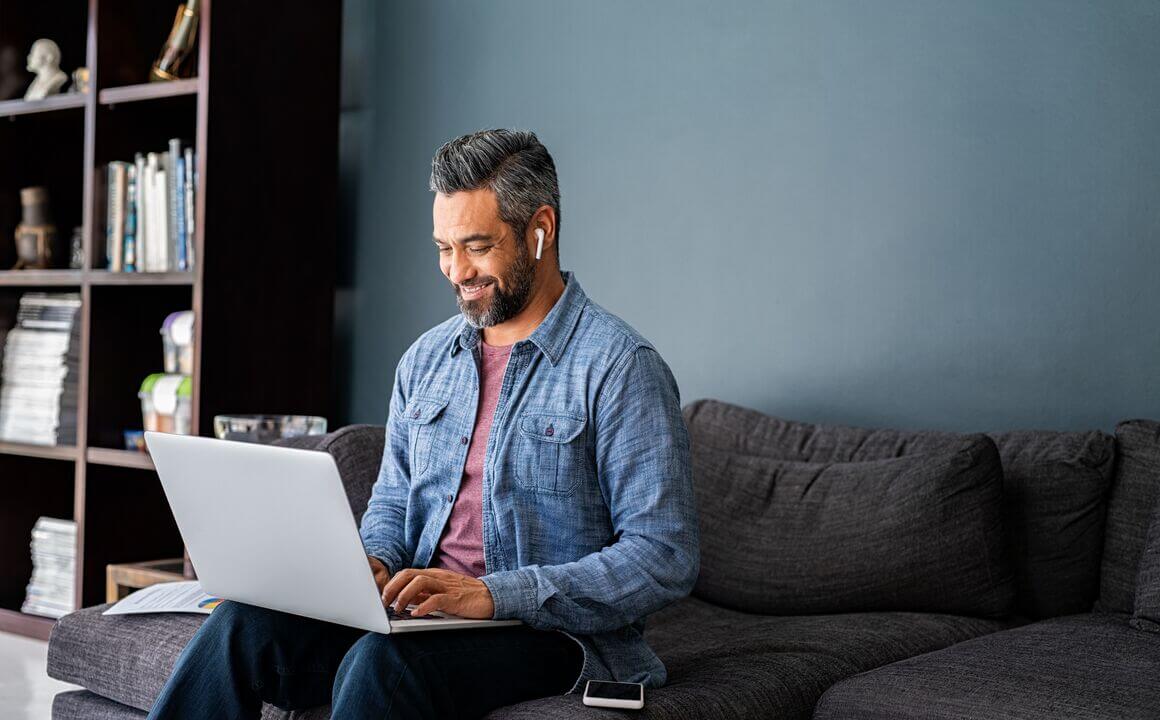 A man sitting with his computer on his lap while wearing earbuds