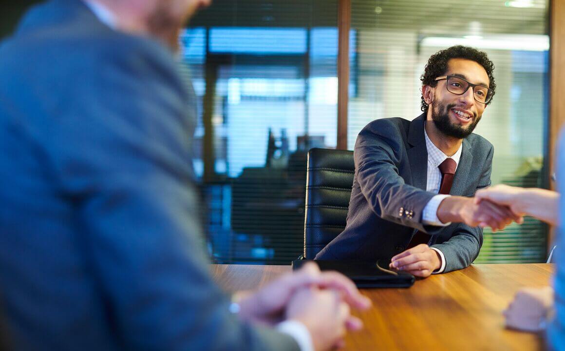 A bearded man shakes hands across an office table