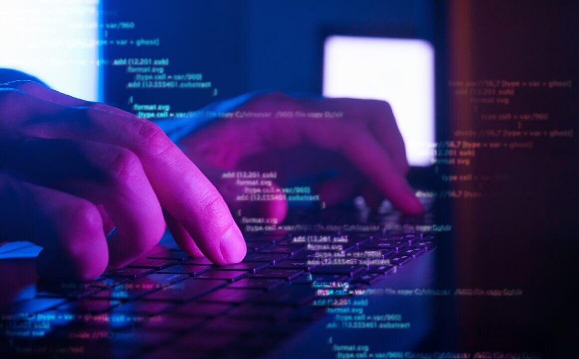 purple light reflects on hands with overlaid computer code 