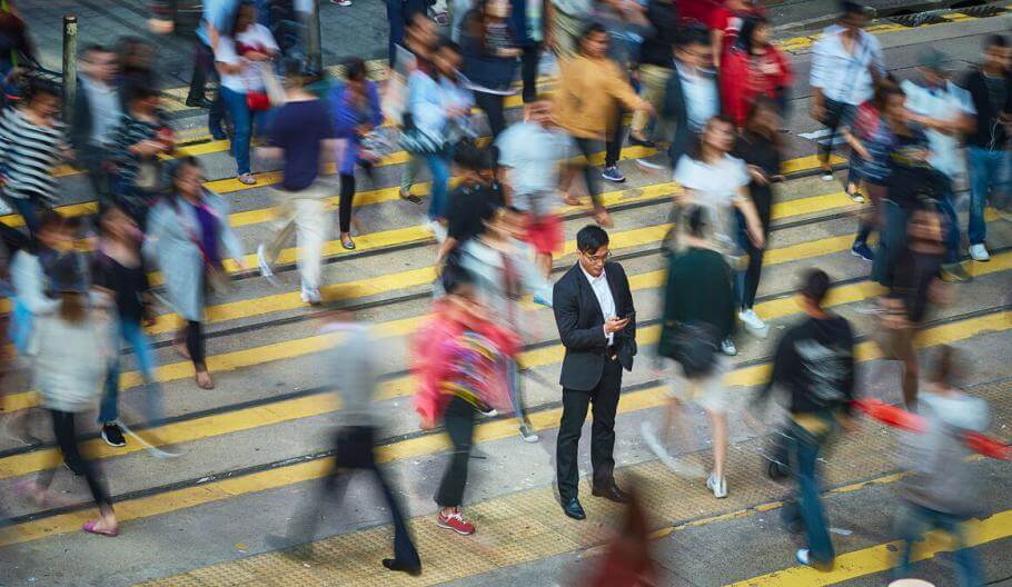 A man checks his phone, still among a blurred crowd
